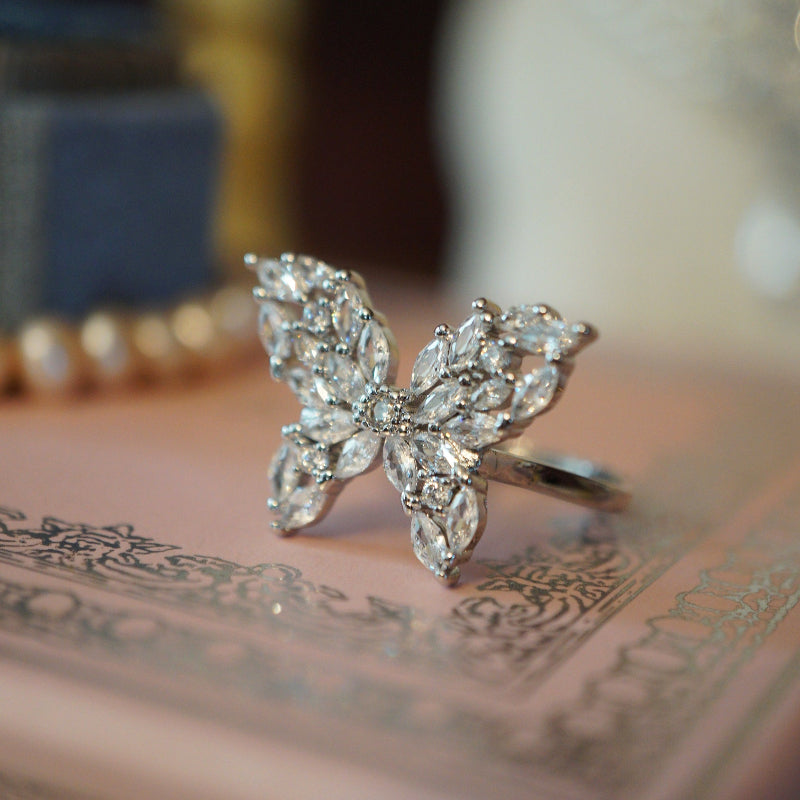 Elegant butterfly ring crafted with marquise and round-cut clear zircons set in an 18K white gold plated band, displayed on a pink decorative surface