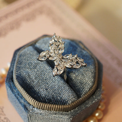 Elegant butterfly ring crafted with marquise and round-cut clear zircons set in an 18K white gold plated band, displayed on a pink decorative surface