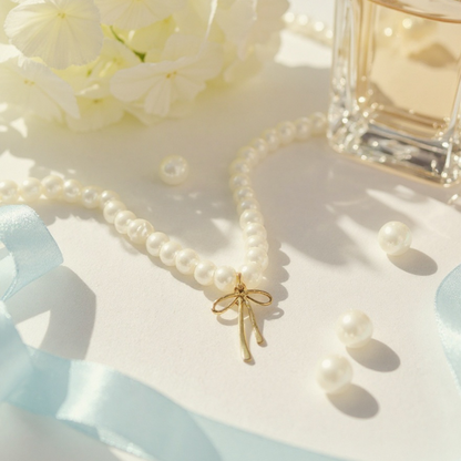 Elegant pearl necklace with gold bow pendant displayed with perfume and blue ribbon background, luxury feminine jewelry product